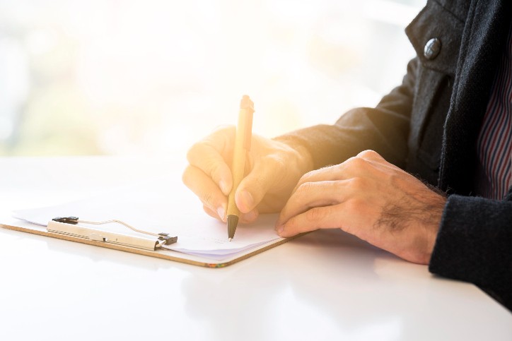 Person signing a document on a clipboard, symbolizing the process of signing up for Original Medicare Parts A and B.