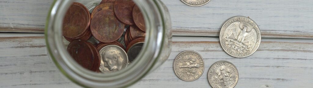 Jar of pennies with scattered coins on a white-wooden surface