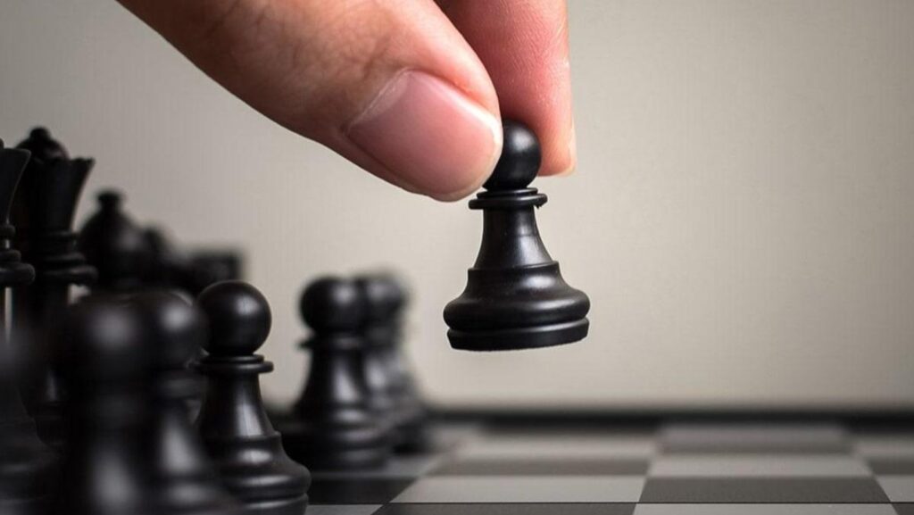 Hand moving a black chess pawn on a chessboard, symbolizing strategic planning in Medicare health insurance